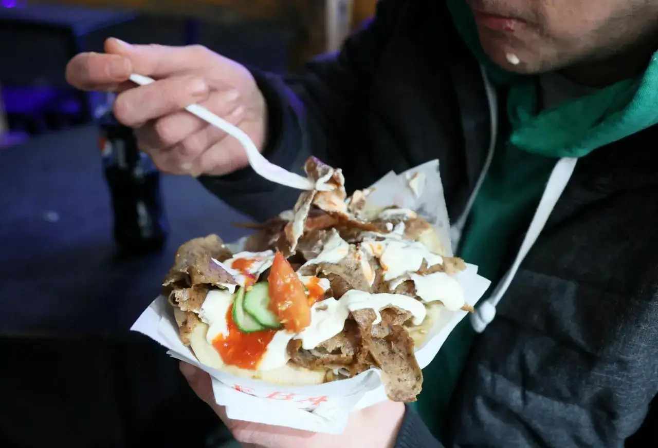 Człowiek je pysznego kebaba z mięsem, warzywami i sosami. Zastanawiasz się, ile kosztuje kebab w Niemczech?