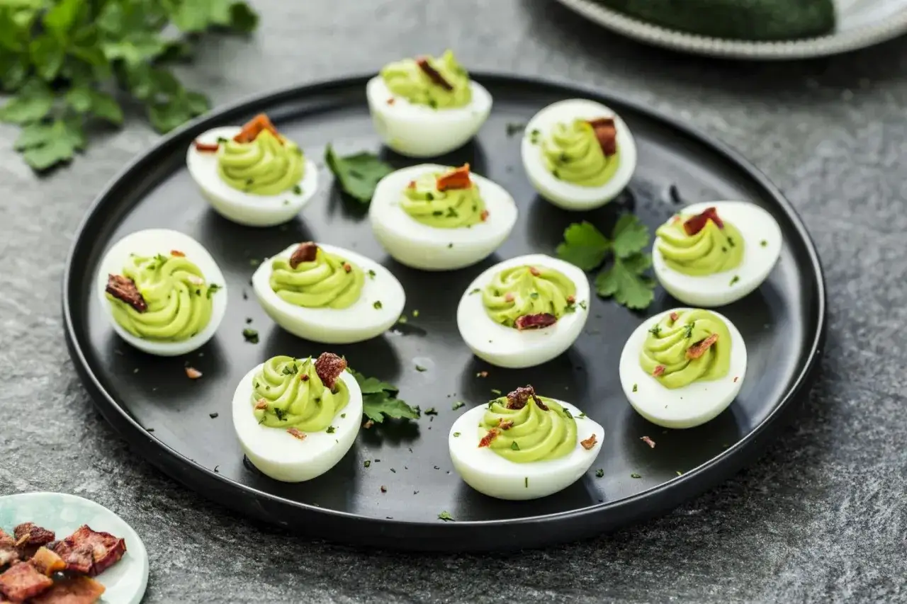 Pyszne jajka faszerowane awokado, udekorowane chrupiącym boczkiem i natką pietruszki, prezentują się apetycznie na czarnym talerzu.