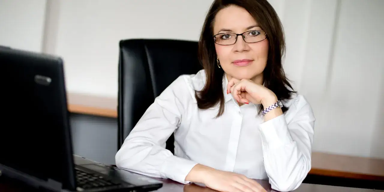 Kobieta w okularach siedzi przy biurku z laptopem. To obraz zawodu przyszłości dla kobiet, pełnego sukcesów i innowacji.