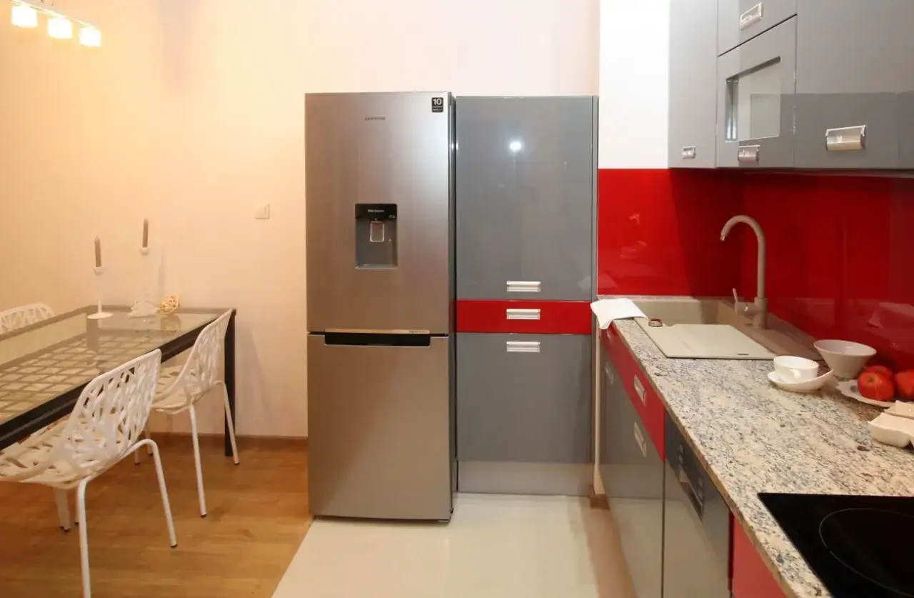 Nowoczesna kuchnia z lodówką Samsung no frost, gotową do pierwszego uruchomienia. Obok niej stół z białymi krzesłami.