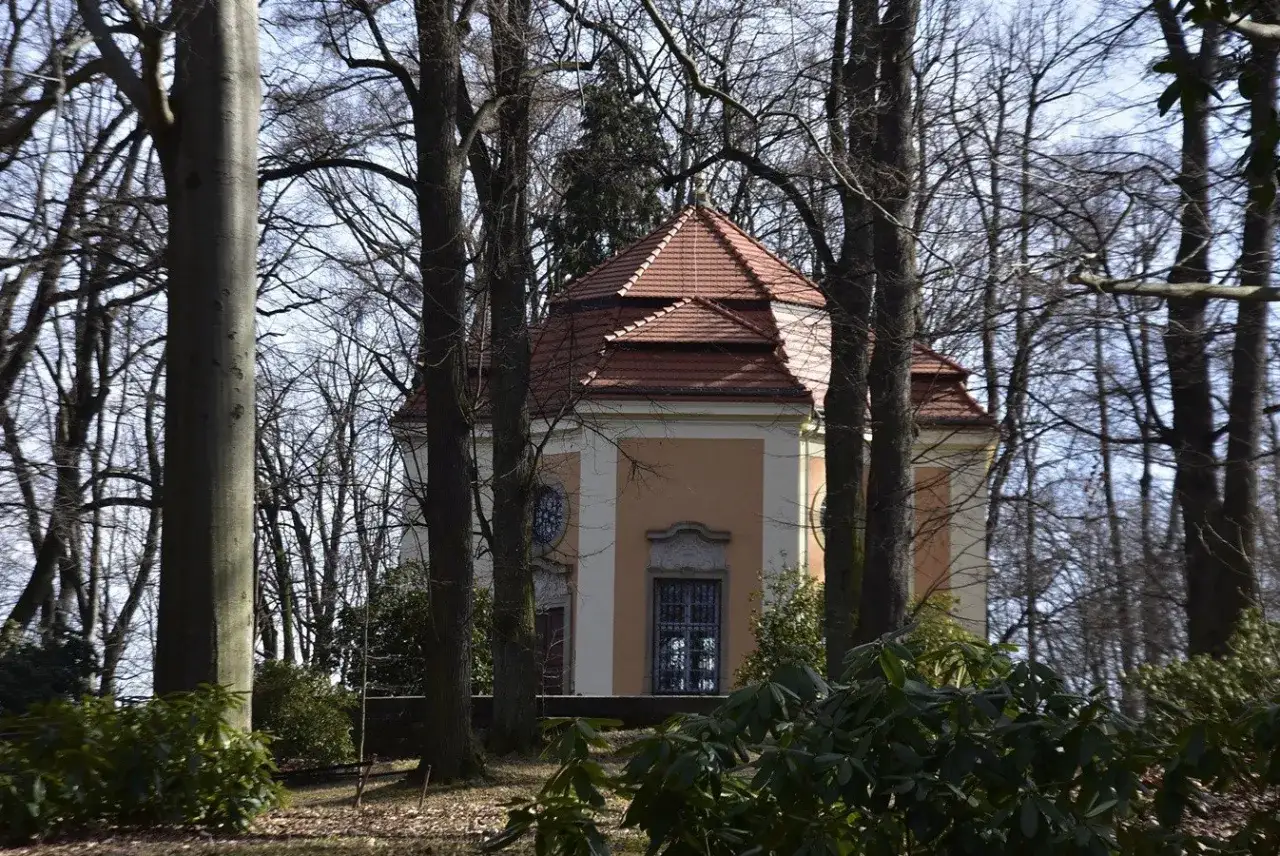 Kaplica w Książańskim Parku Krajobrazowym, otoczona drzewami, z charakterystycznym, wielospadowym dachem.