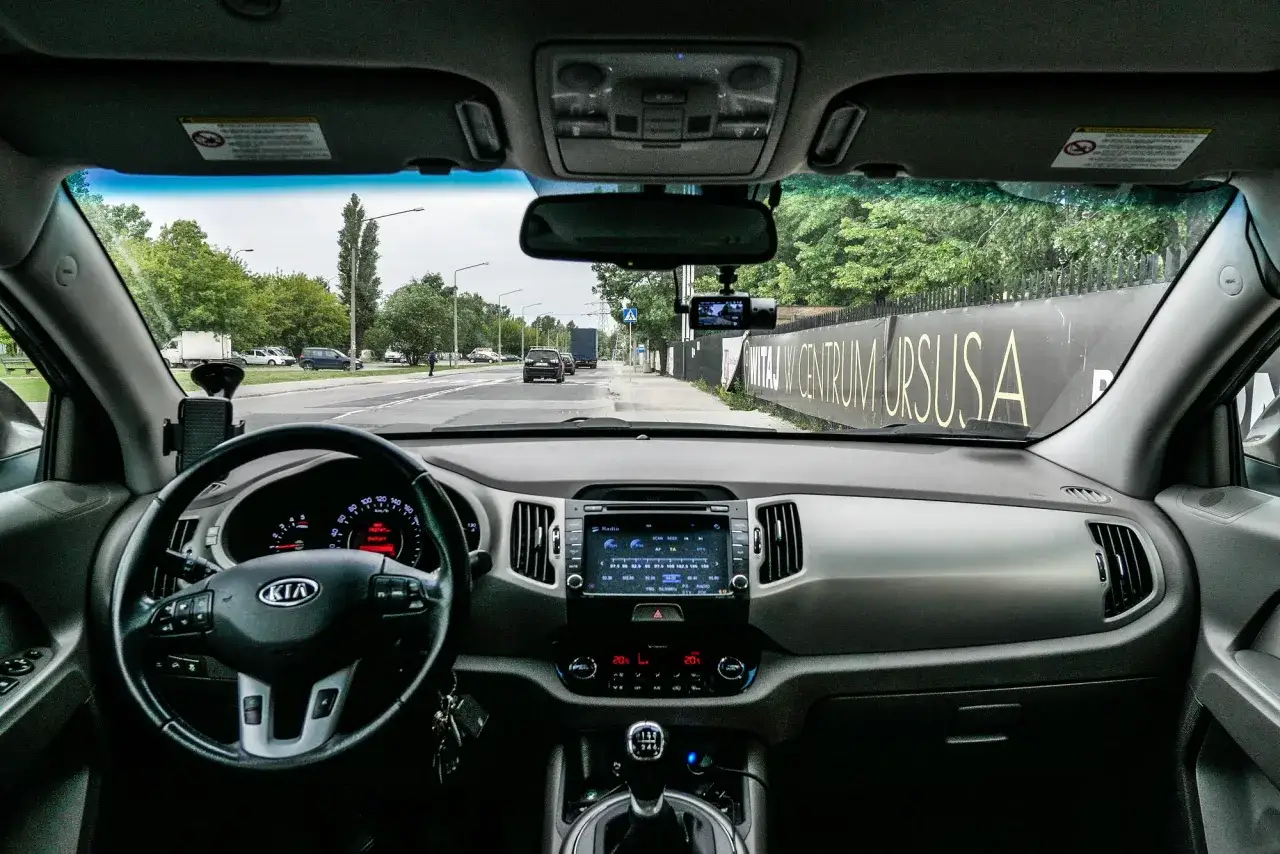 Widok z wnętrza samochodu na deskę rozdzielczą i drogę. Na szybie zamontowany wideorejestrator, który pokazuje, jak podłączyć wideorejestrator.