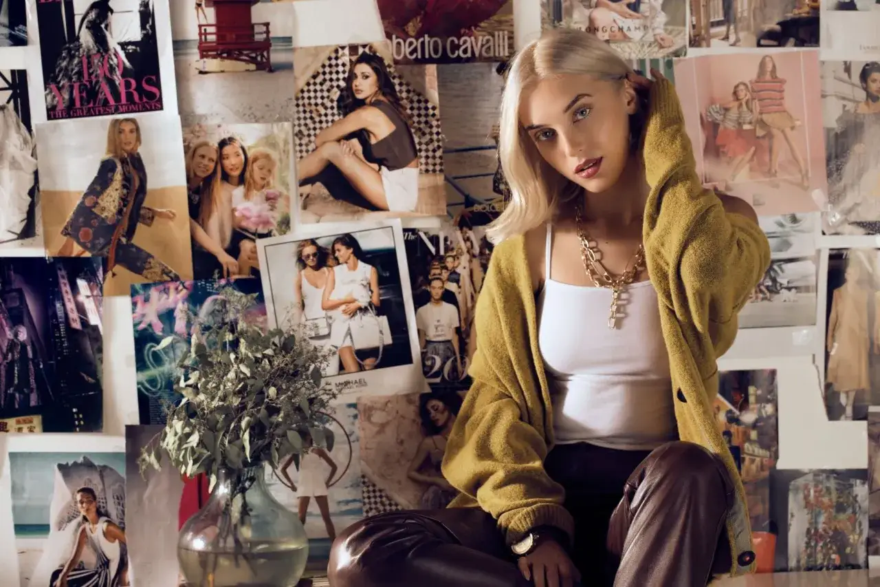Młoda kobieta w musztardowym kardiganie i skórzanych spodniach na tle kolażu z pracami słynnych projektantów mody.
