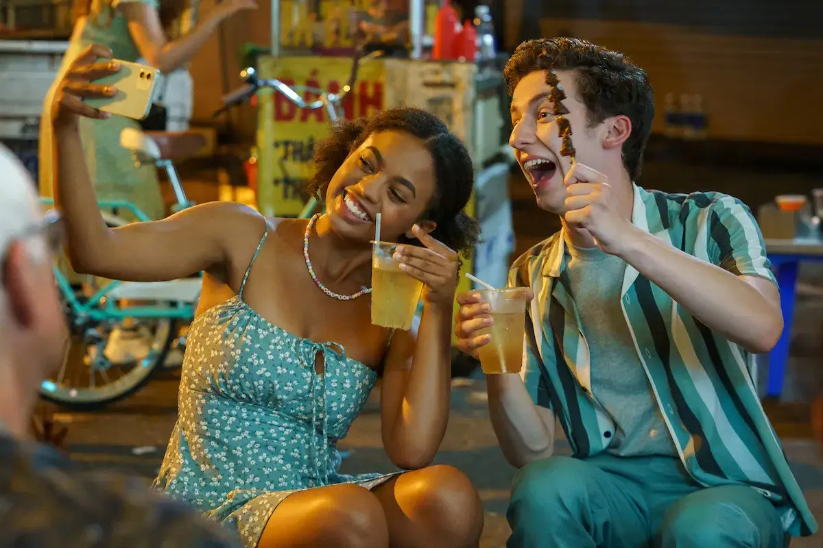 Uśmiechnięta para robi selfie z napojami i jedzeniem na patyku. To ich przewodnik po miłości i wsp&oacute;lnych chwilach.