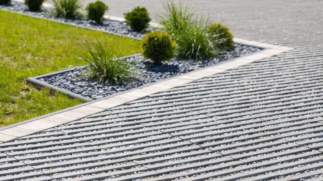 Nowoczesny podjazd z płyt betonowych, wypełniony żwirem, otoczony zielenią i kamieniami.