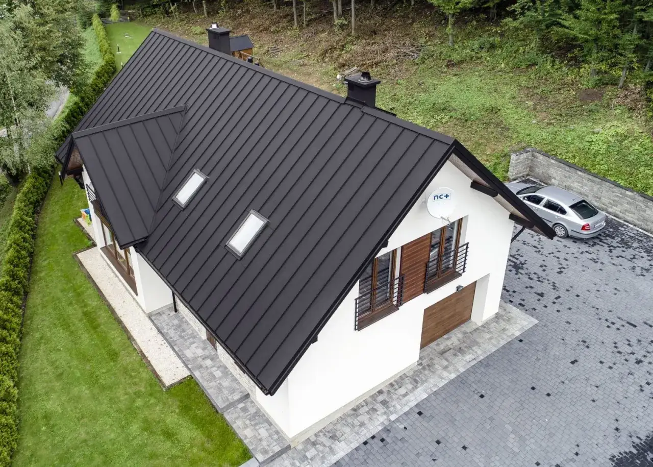 Nowoczesny dom z czarnym dachem z blachy na rabek, otoczony zielenią.