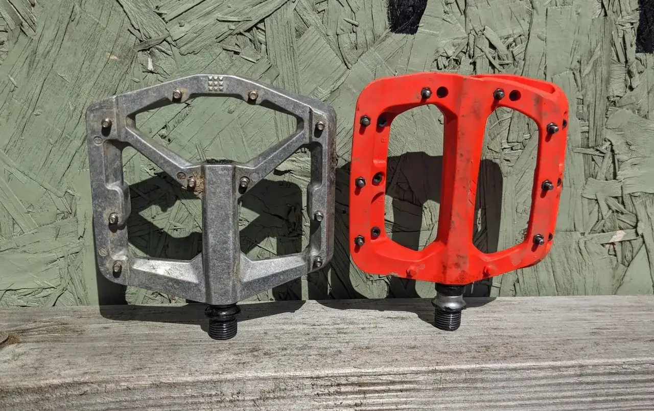 Dwa pedały rowerowe, jeden srebrny, drugi czerwony, z pinami. Idealne, jeśli zastanawiasz się, jakie pedały do gravela wybrać.