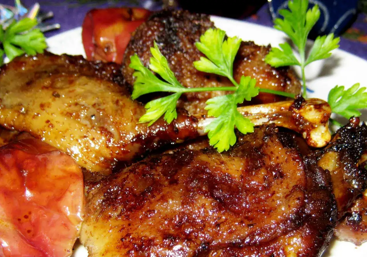 Apetyczna kaczka pieczona w kawałkach, z rumianą sk&oacute;rką i jabłkami, ozdobiona natką pietruszki.