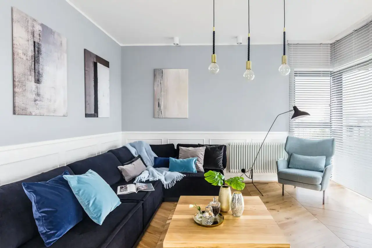 Szare ściany i ciemna sofa to świetny pomysł na pomalowanie pokoju. Jasne dodatki i obrazy dodają lekkości.