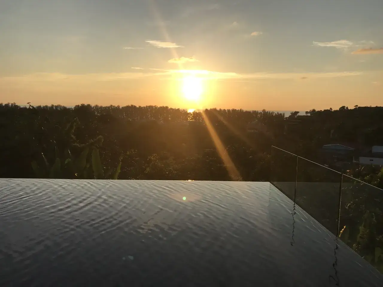 Zachód słońca nad tropikalną roślinnością i basenem infinity. Idealny czas, by pomyśleć, kiedy jechać na Phuket.