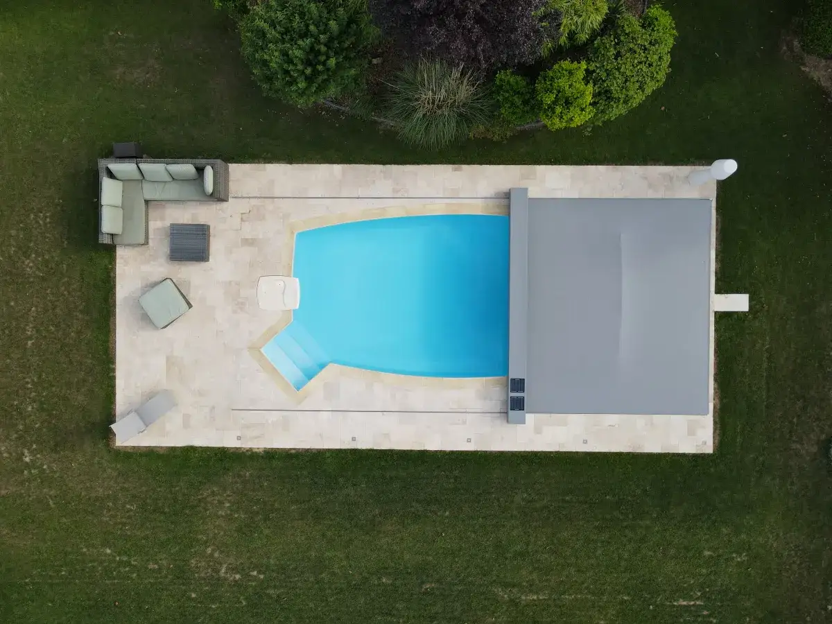 Widok z lotu ptaka na mały basen z niebieską wodą, schodkami i szarym przykryciem. Obok meble ogrodowe. Zastanawiasz się, ile kosztuje budowa małego basenu?