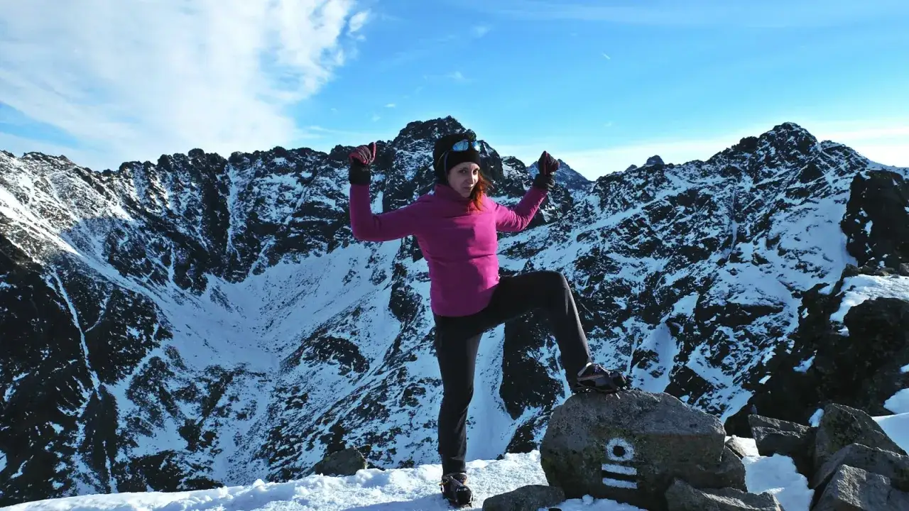 Kobieta na szczycie Kościelca zimą, dumna z pokonania górskich szlaków.
