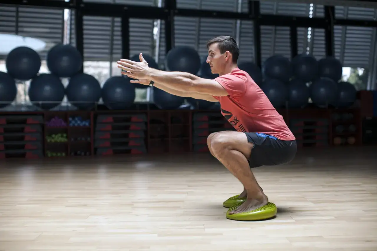 Mężczyzna wykonuje przysiady na poduszkach balansowych, wzmacniając ćwiczenia na mięśnie głębokie.