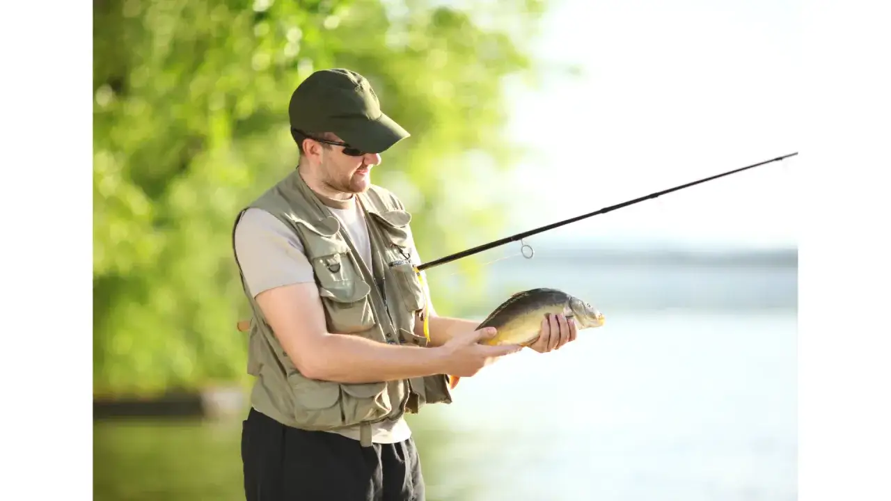 Wędkarz z karpiem w ręku i wędką. Czy można łowić ryby bez karty wędkarskiej? To pytanie zadaje sobie wielu hobbystów.