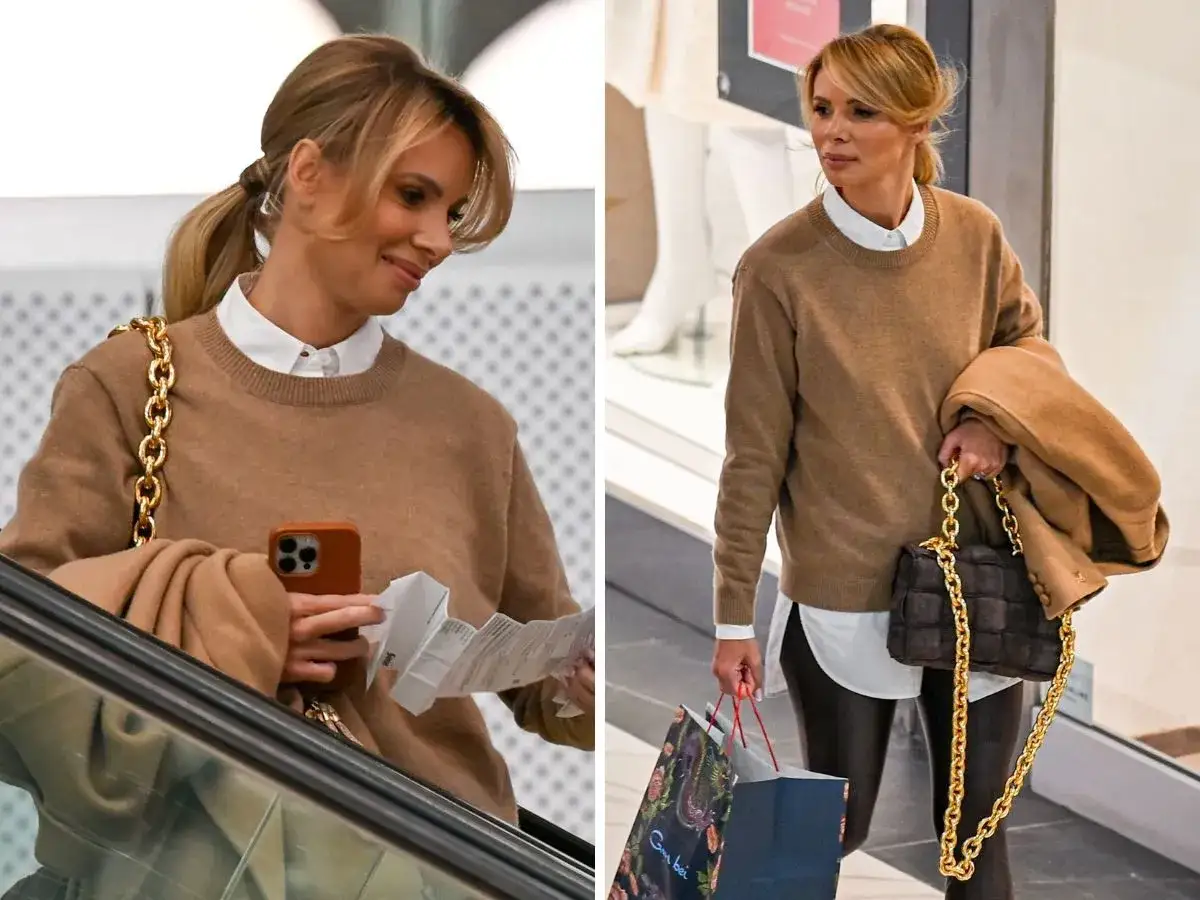 Izabela Janachowska-Jabłońska w brązowym swetrze i z elegancką torebką, z telefonem i paragonem w ręku, na schodach ruchomych.