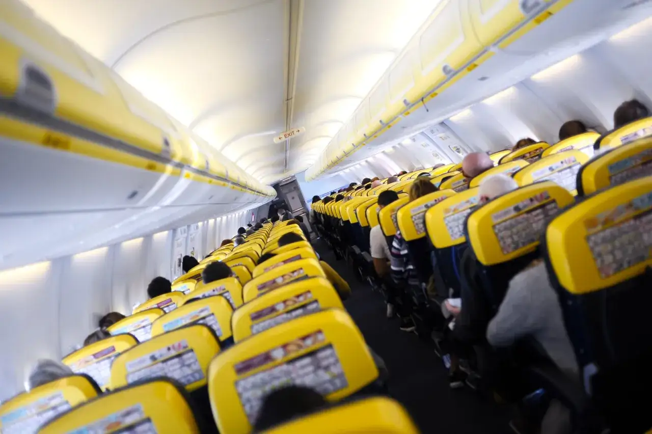 Wnętrze samolotu z żółtymi siedzeniami. Pasażerowie czekają na start. Zastanawiasz się, ile trwa lot z Warszawy do Katanii?