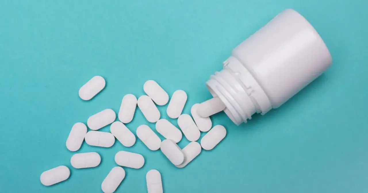 Białe tabletki rozsypane z białego pojemnika. Flunarizinum na co? Na migrenę, zawroty głowy.