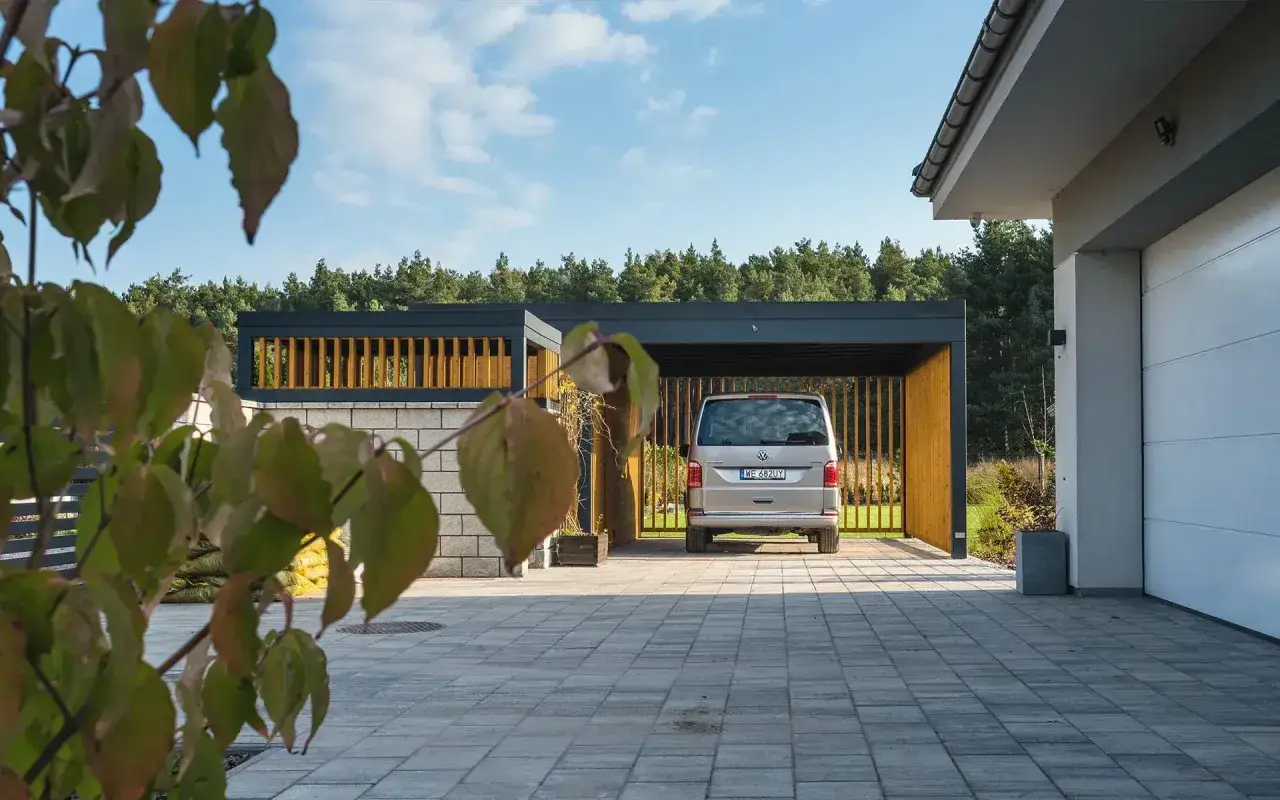 Nowoczesna wiata z drewnianymi elementami, gdzie zaparkował srebrny bus. Czy na taką konstrukcję potrzebne jest pozwolenie na budowę czy zgłoszenie?