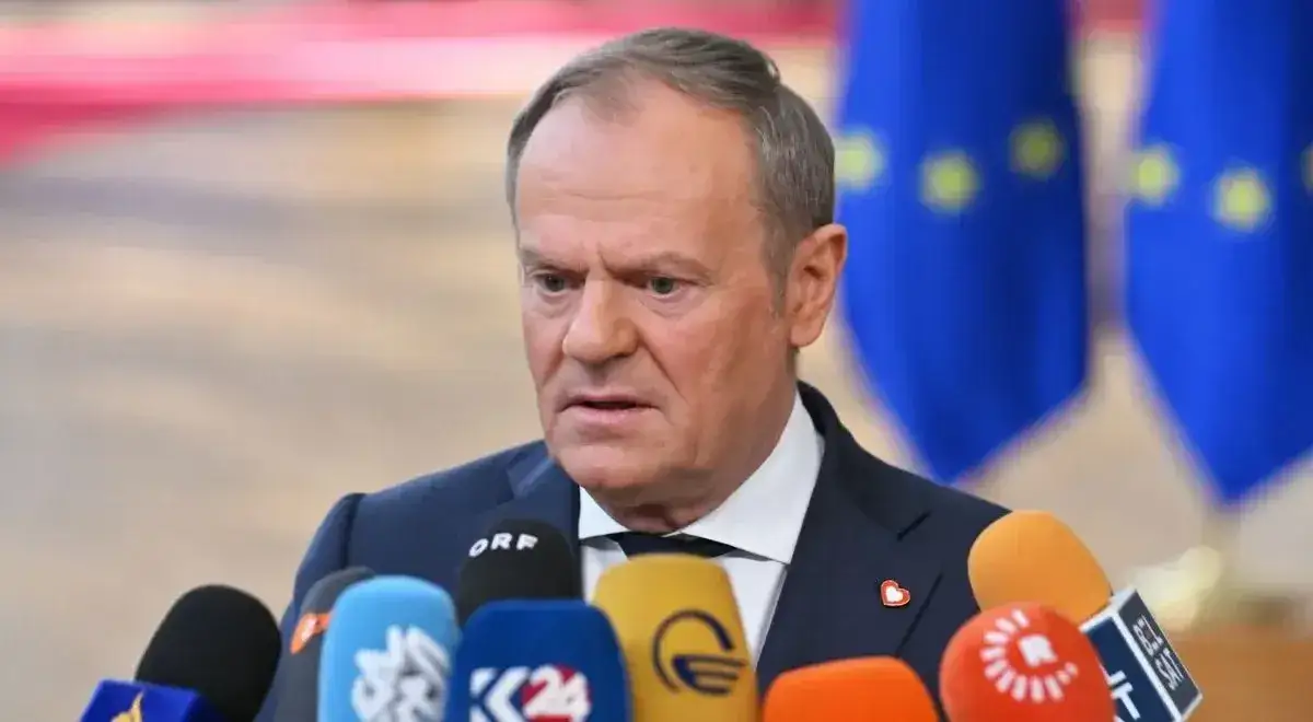 Donald Tusk przed mikrofonami, otoczony flagami UE. Czy Tusk zna angielski? Pytanie pozostaje otwarte, gdy polityk przemawia.
