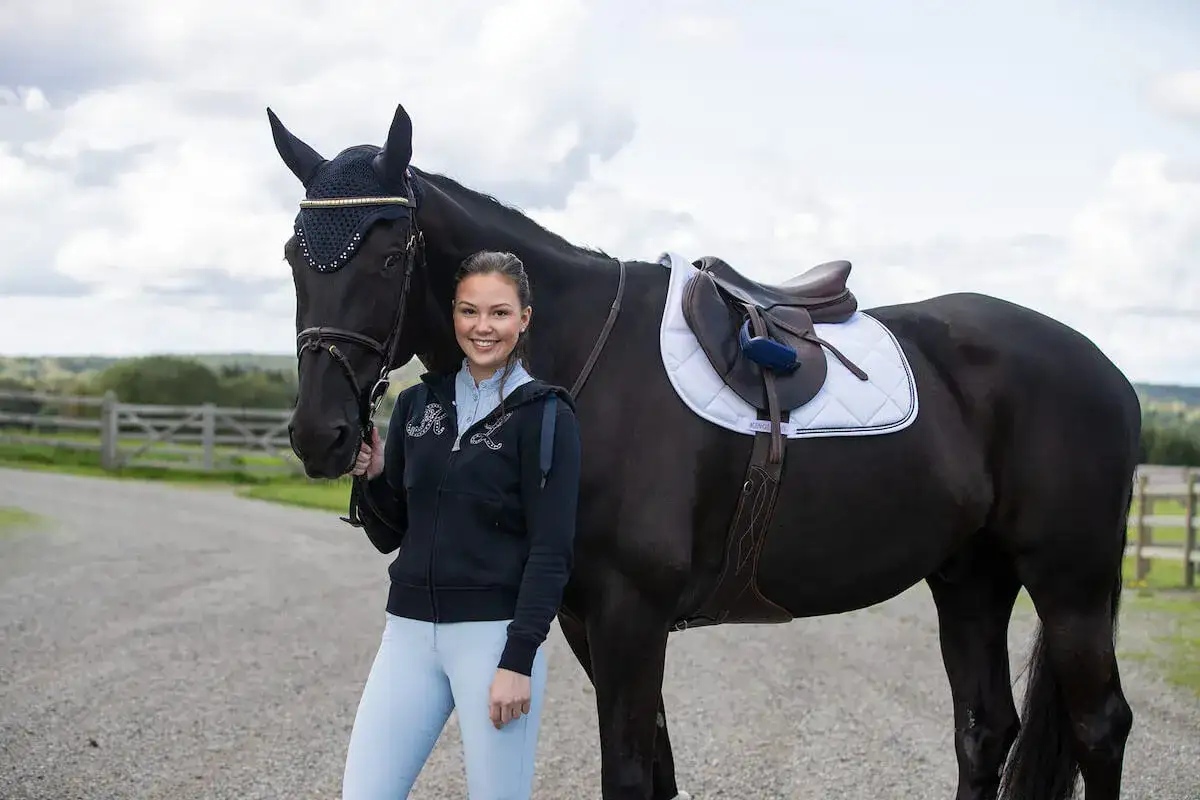 Uśmiechnięta jeźdźczyni z czarnym koniem. Zastanawiasz się, ile kosztuje czaprak? Ten biały, pikowany, z brązową lamówką, wygląda na drogi.
