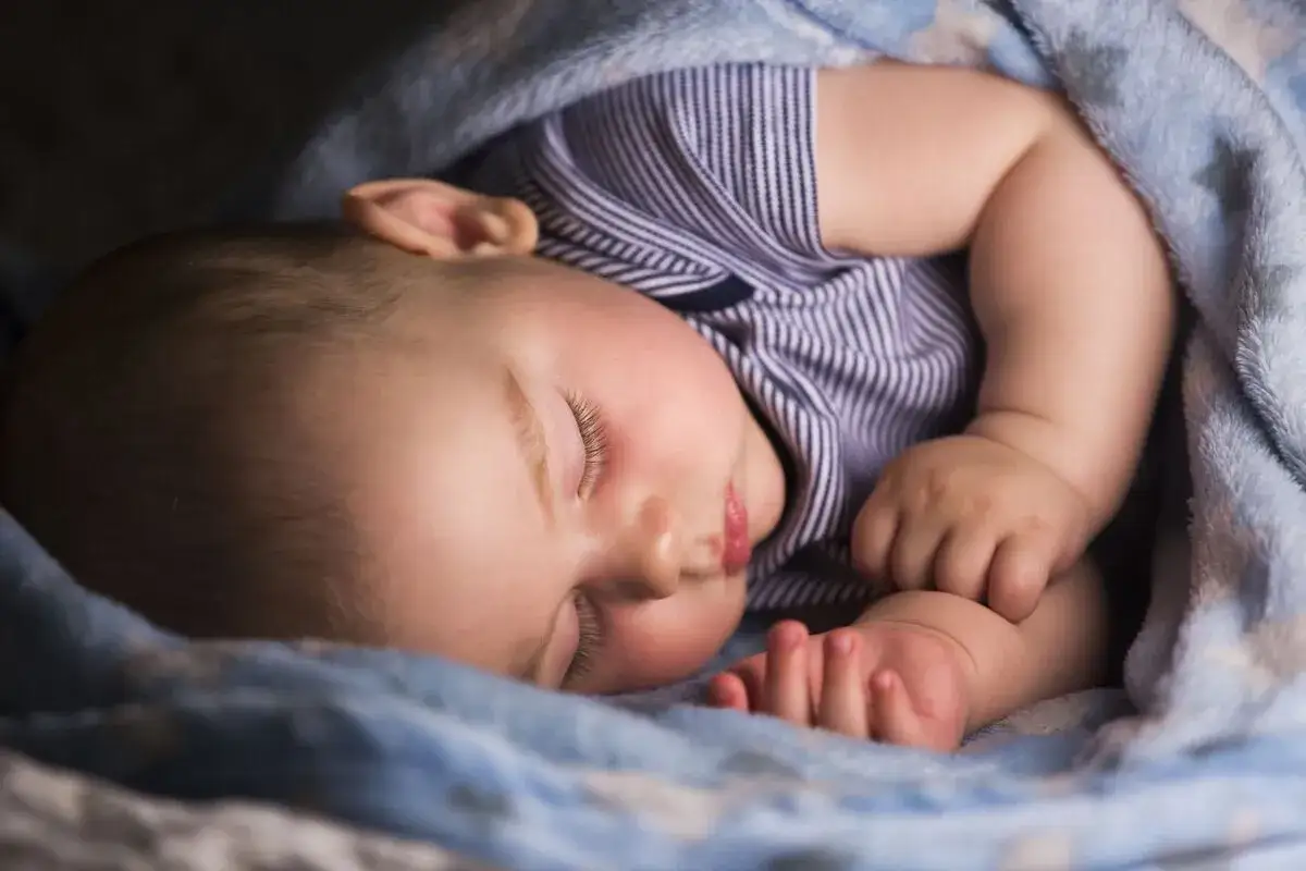 Śpiące dziecko otulone kocykiem. Warto wiedzieć, jak pomóc dziecku przy ząbkowaniu w nocy, by zapewnić mu spokojny sen.