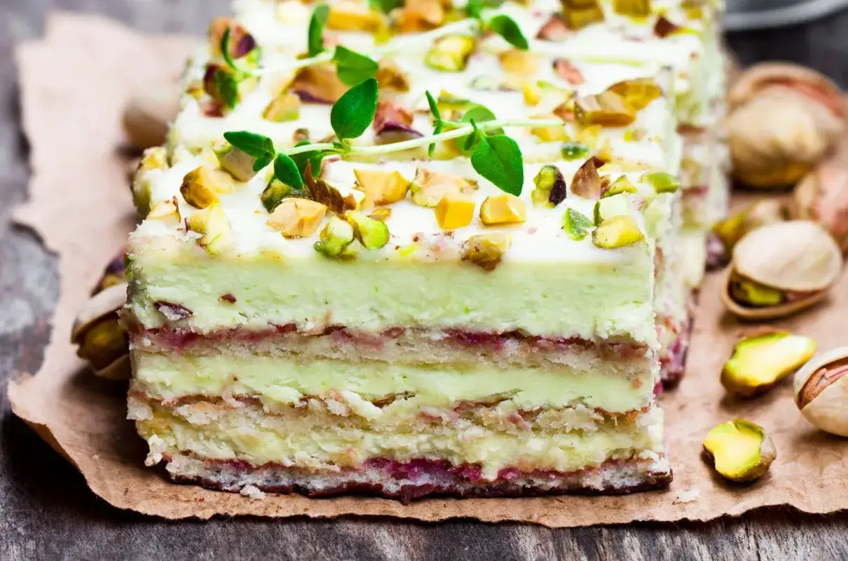 Pyszny tort z warstwami biszkoptu i kremu, ozdobiony posiekanymi pistacjami. W środku wyczuwalna masa pistacjowa i delikatna konfitura.