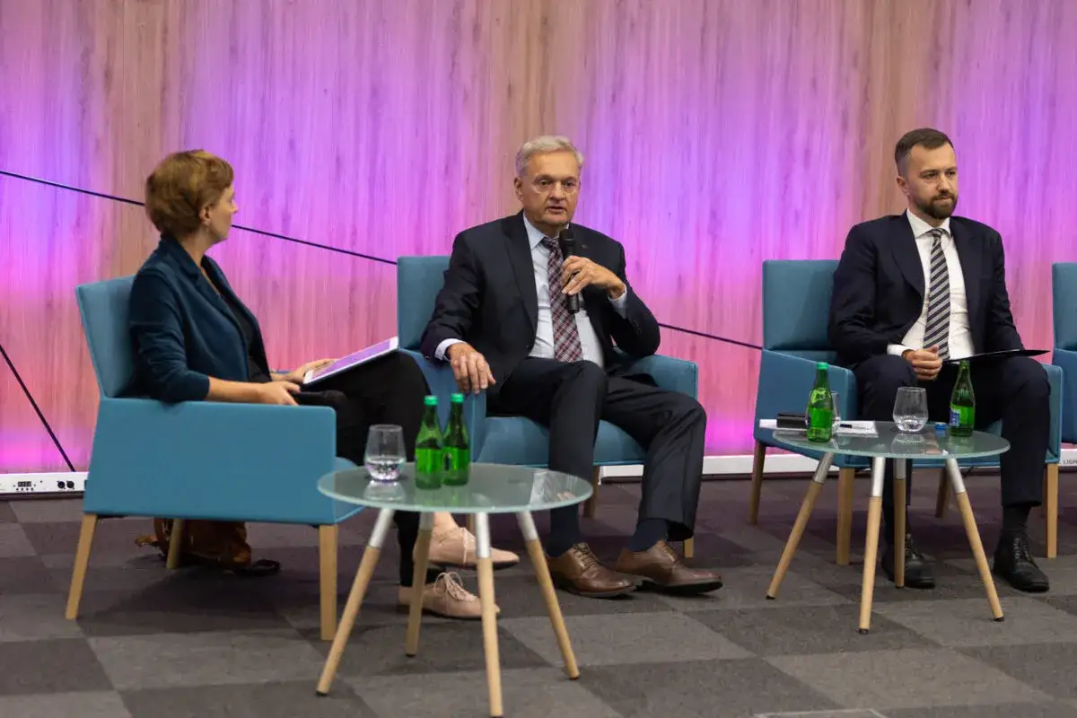 Dyskusja panelowa z udziałem osoby zaufania publicznego. Trzy osoby siedzą na krzesłach, przed nimi stoliki z wodą.