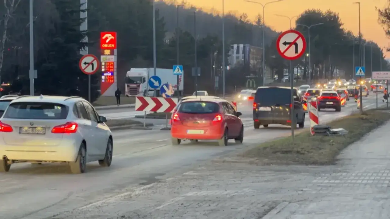 Natężenie ruchu Gdynia: sznur samochodów na drodze, znaki zakazu skrętu, stacja Orlen i McDonald's w tle.