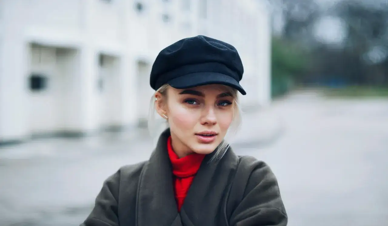 Młoda kobieta w czapce z daszkiem i czerwonym golfie, tworząca stylowe czapka z daszkiem stylizacje.