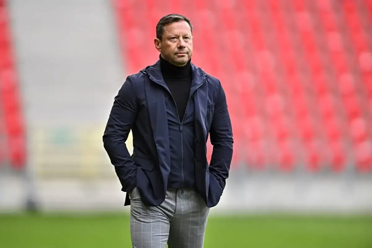 Trener Arki Gdynia w eleganckim stroju, w tle czerwone trybuny. Czy to zapowiedź nowych, ekscytujących pogłosek transferowych?