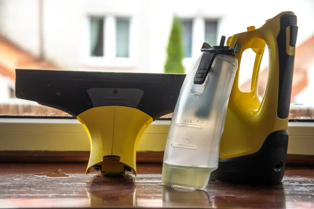 Czy myjka do okien Karcher zostawia smugi przez zużyte gumy czy zły płyn? Na zdjęciu widać żółto-czarną myjkę Karcher z pojemnikiem na płyn, stojącą na drewnianym parapecie.