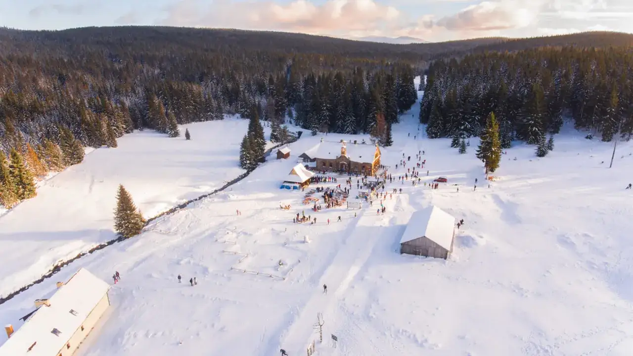 Zimowy dzień w stacji turystycznej Orle. Ludzie spacerują i jeżdżą na nartach po ośnieżonych stokach, otoczonych lasem.