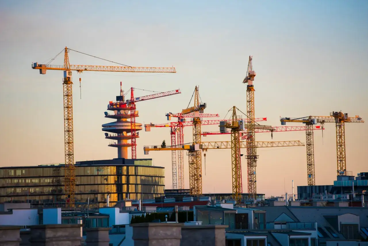 Wielkie żurawie wieżowe na tle zachodzącego słońca, gotowe do pracy dla każdego operatora żurawia wieżowego.