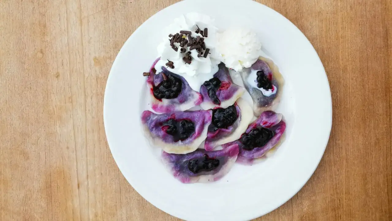 Pyszne pierogi z jagodami, podane z bitą śmietaną, lodami i posypką czekoladową. Letnia uczta na talerzu.