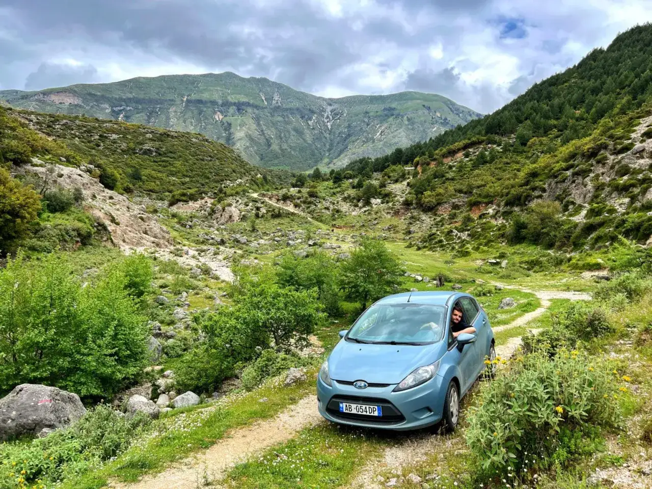 Niebieski samoch&oacute;d na wyboistej drodze w g&oacute;rach Albanii. Podr&oacute;ż przez dziką przyrodę.