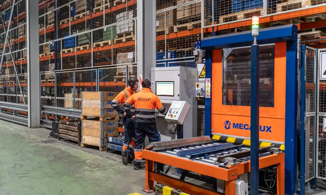 Dw&oacute;ch pracownik&oacute;w w pomarańczowych kamizelkach obserwuje maszynę w magazynie. Zasada genchi genbutsu w praktyce &ndash; zrozumienie procesu przez obserwację.