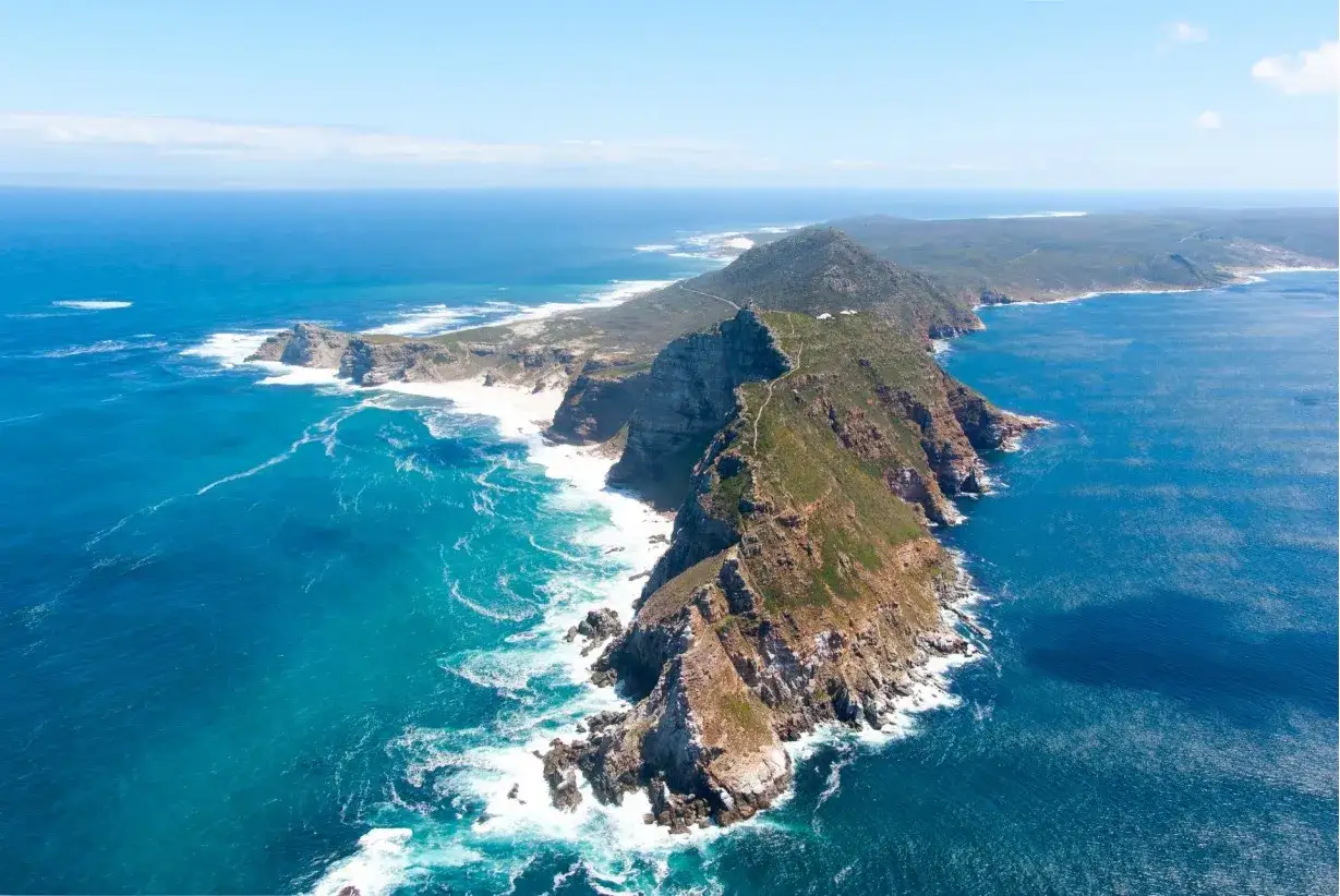 Przylądek Dobrej Nadziei, skaliste wybrzeże z zielenią, turkusowe morze i białe fale rozbijające się o brzeg.