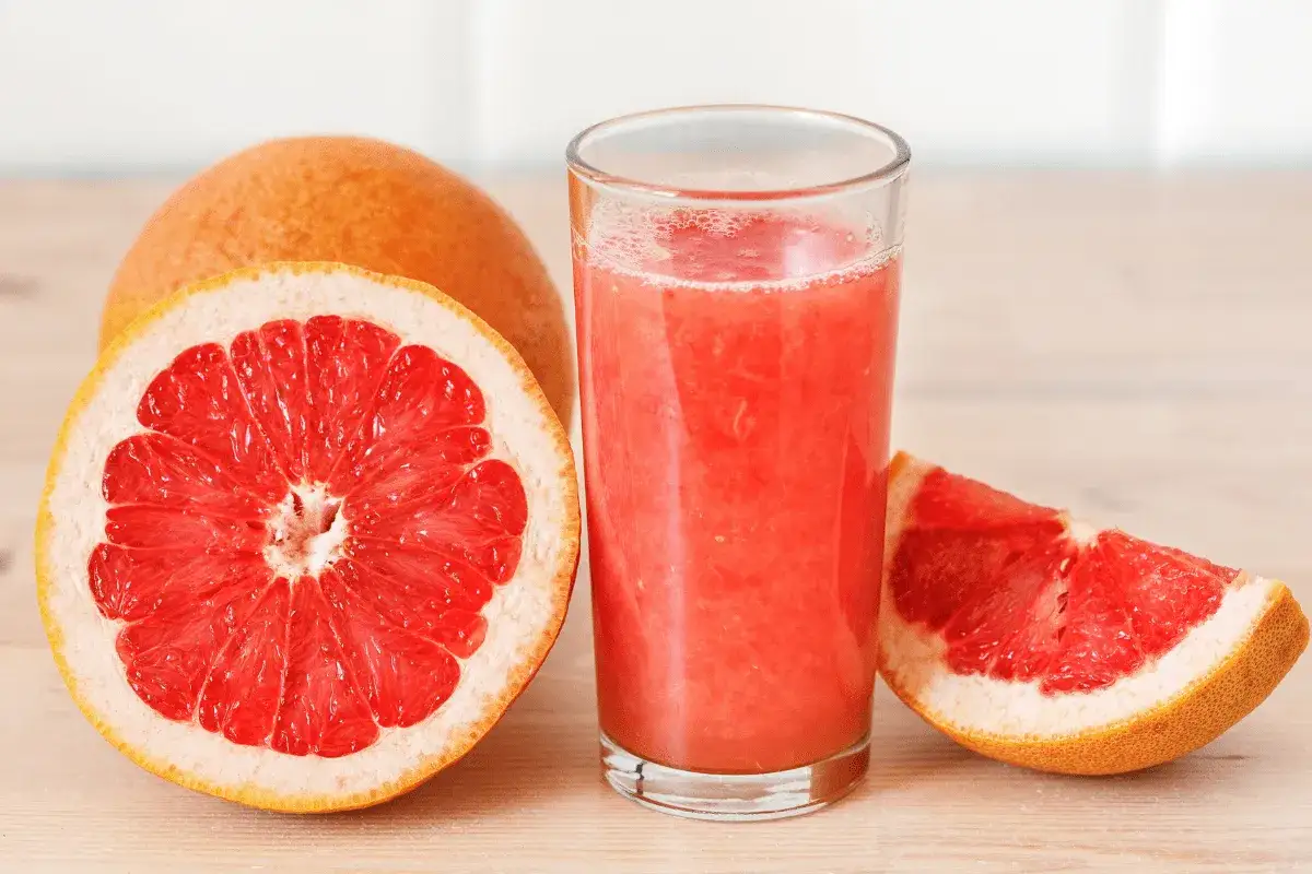 Szklanka soku grejpfrutowego obok przekrojonego owocu i ćwiartki. Pamiętaj o interakcjach soku grejpfrutowego z lekami.