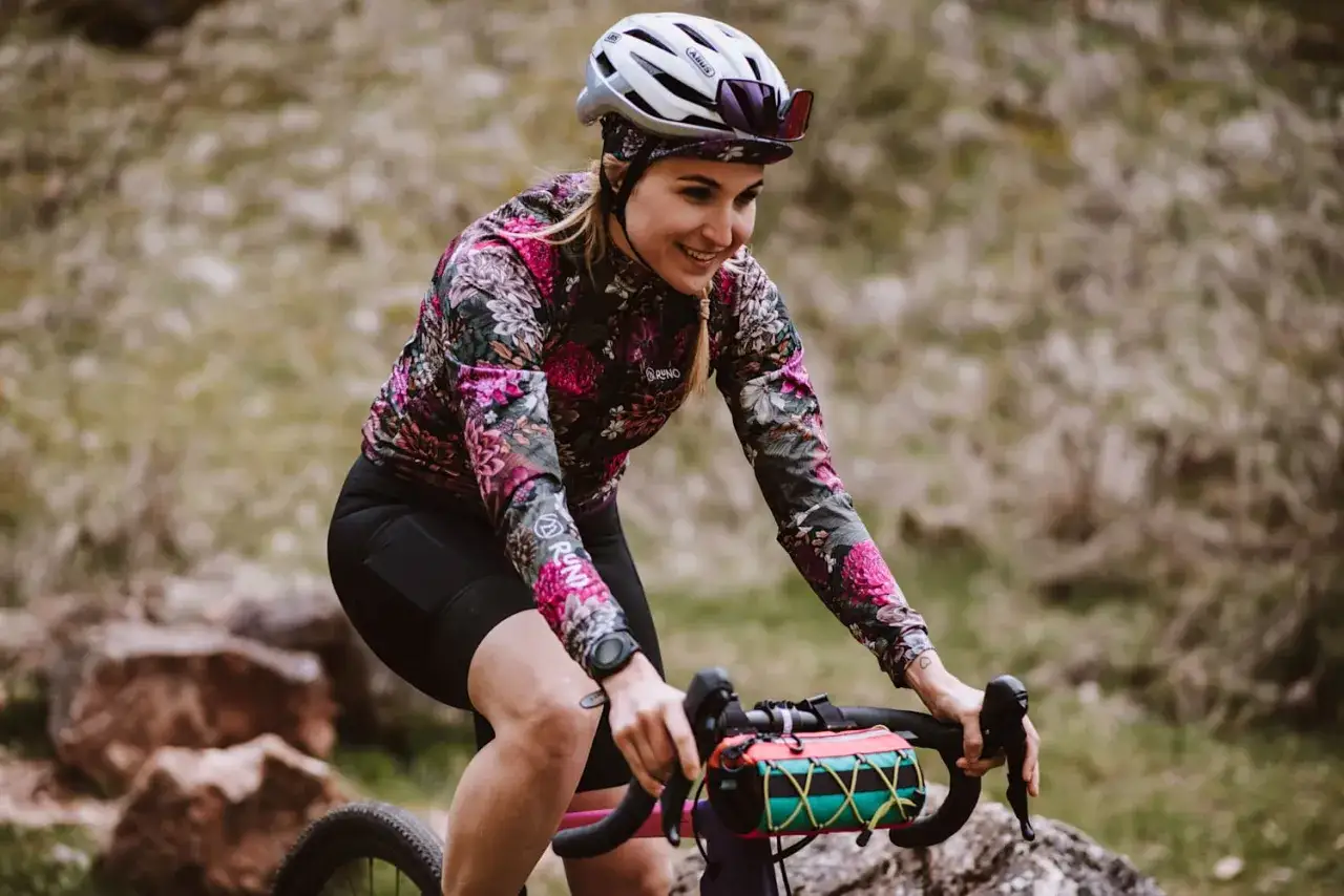 Uśmiechnięta rowerzystka w kwiecistej bluzce pokonuje kolejne kilometry. Dziś cel to 50 km na rowerze po malowniczych terenach.