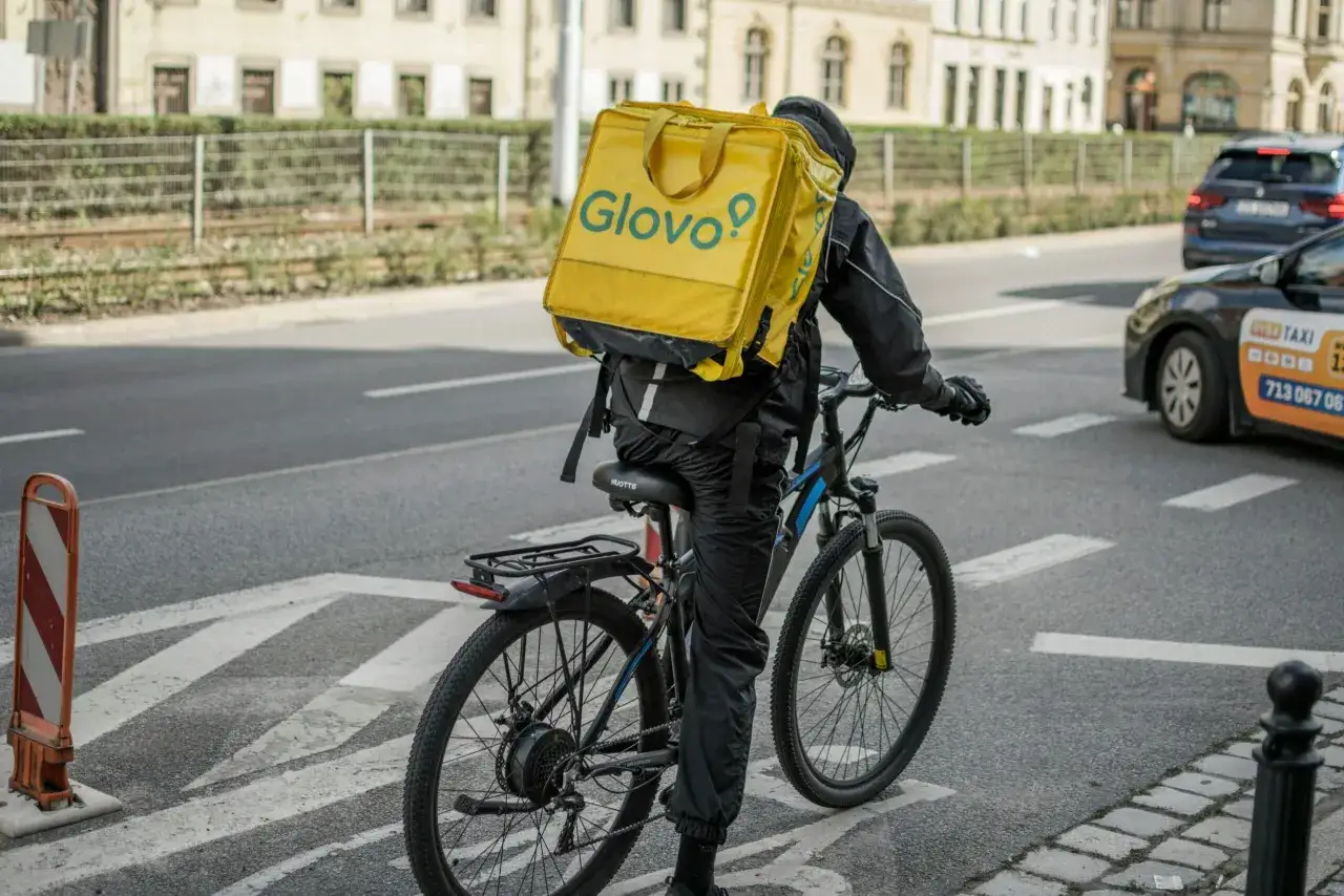 Kurier Glovo na rowerze z żółtą torbą. Zastanawiasz się, ile zarabia pracownik Glovo?