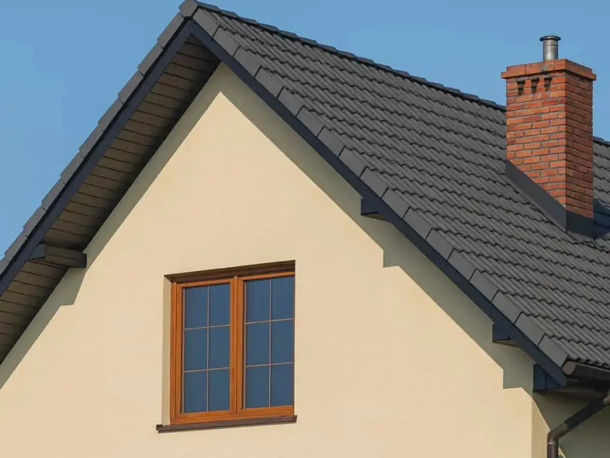Wykończenie ściany szczytowej domu z oknem i ceglanym kominem pod błękitnym niebem.