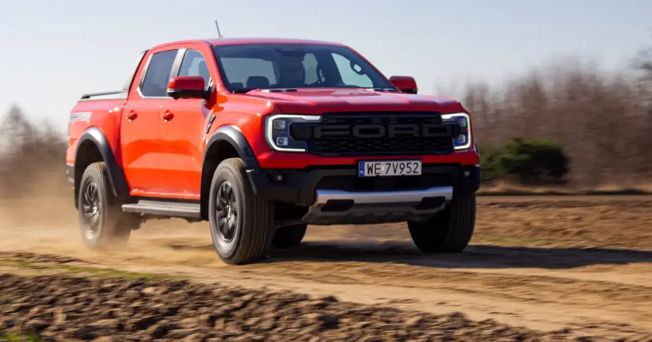 Czerwony Ford Raptor pędzi po piaszczystej drodze, wzbijając kurz. Choć jego moc robi wrażenie, warto pamiętać o kwestii ford raptor spalanie.