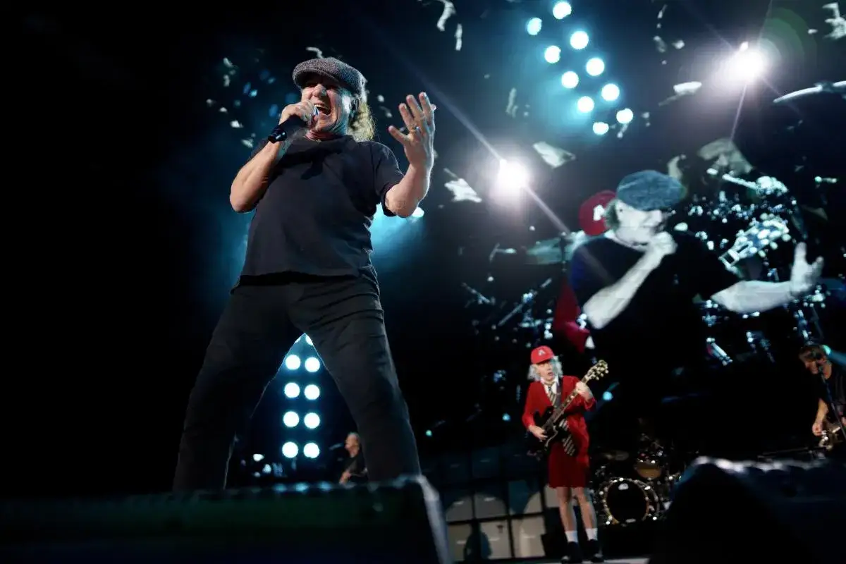 Brian Johnson z AC/DC na scenie, w tle Angus Young w czerwonej marynarce. Koncertowy skład AC/DC w akcji.
