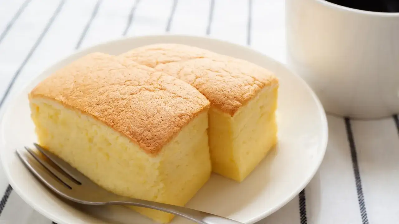 Dwa puszyste kawałki japońskiego ciasta gąbka na talerzyku, obok filiżanki kawy. Zastanawiasz się, ile kcal ma japońskie ciasto gąbka?