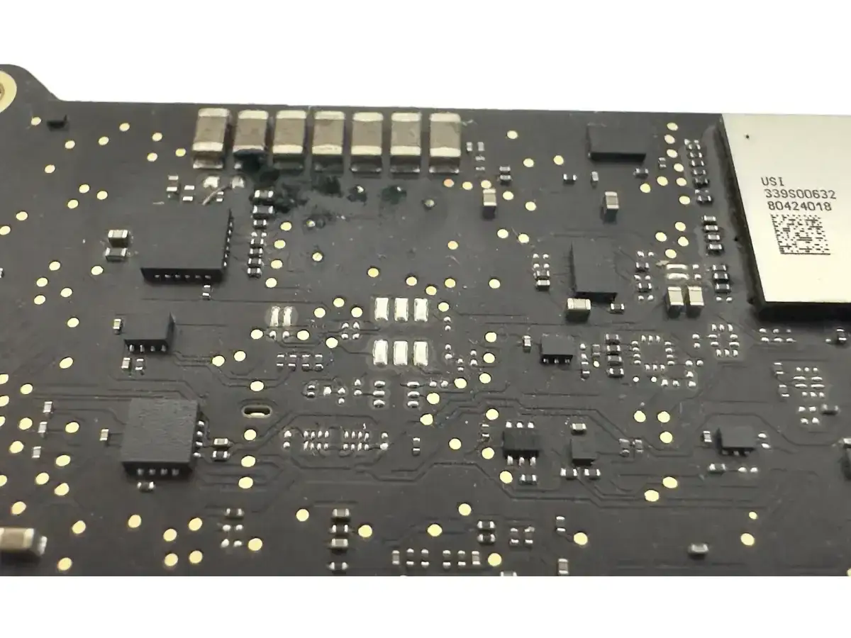 Płyta główna MacBooka, która nie włącza się. Widoczne ślady przepalenia przy kondensatorach.