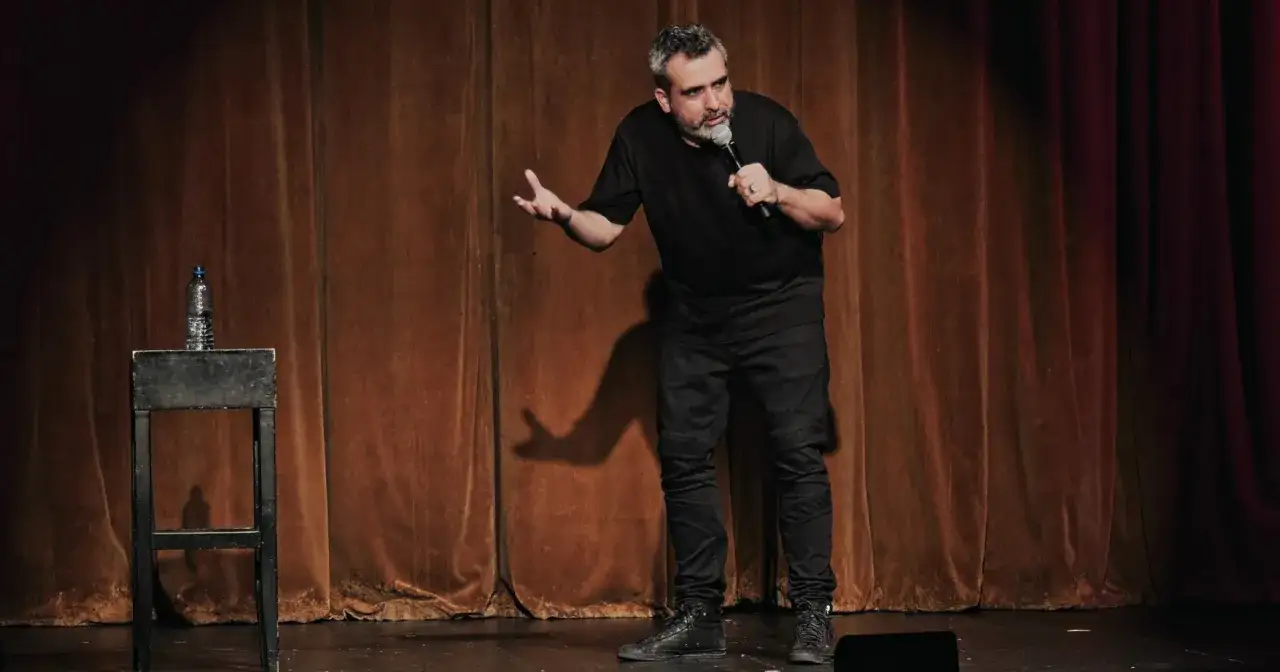 Abelard Giza stand up na scenie, opowiadając dowcipy do mikrofonu.