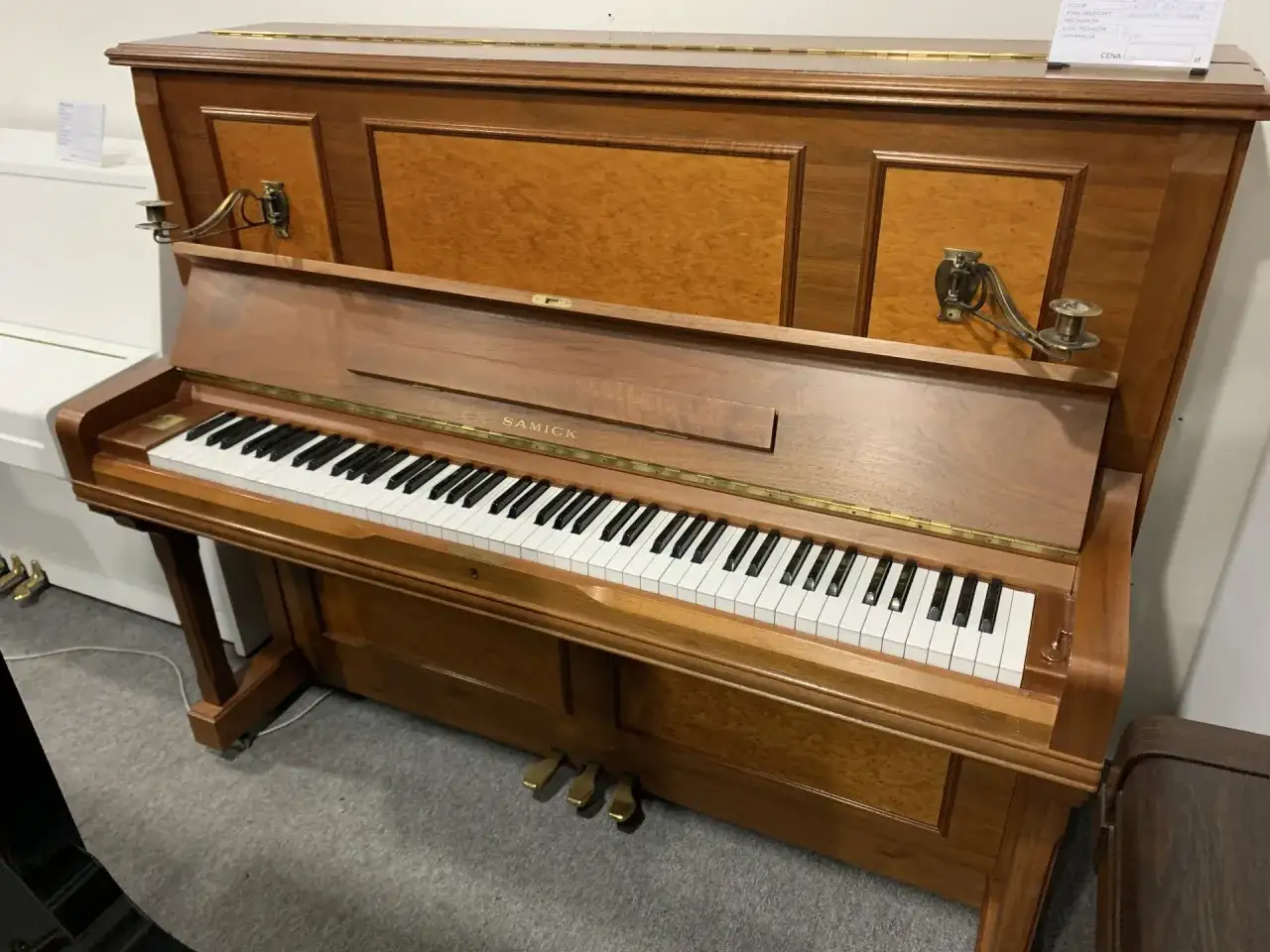 Drewniane pianino pionowe, klasyczne instrumenty muzyczne, z ozdobnymi świecznikami i klawiaturą.
