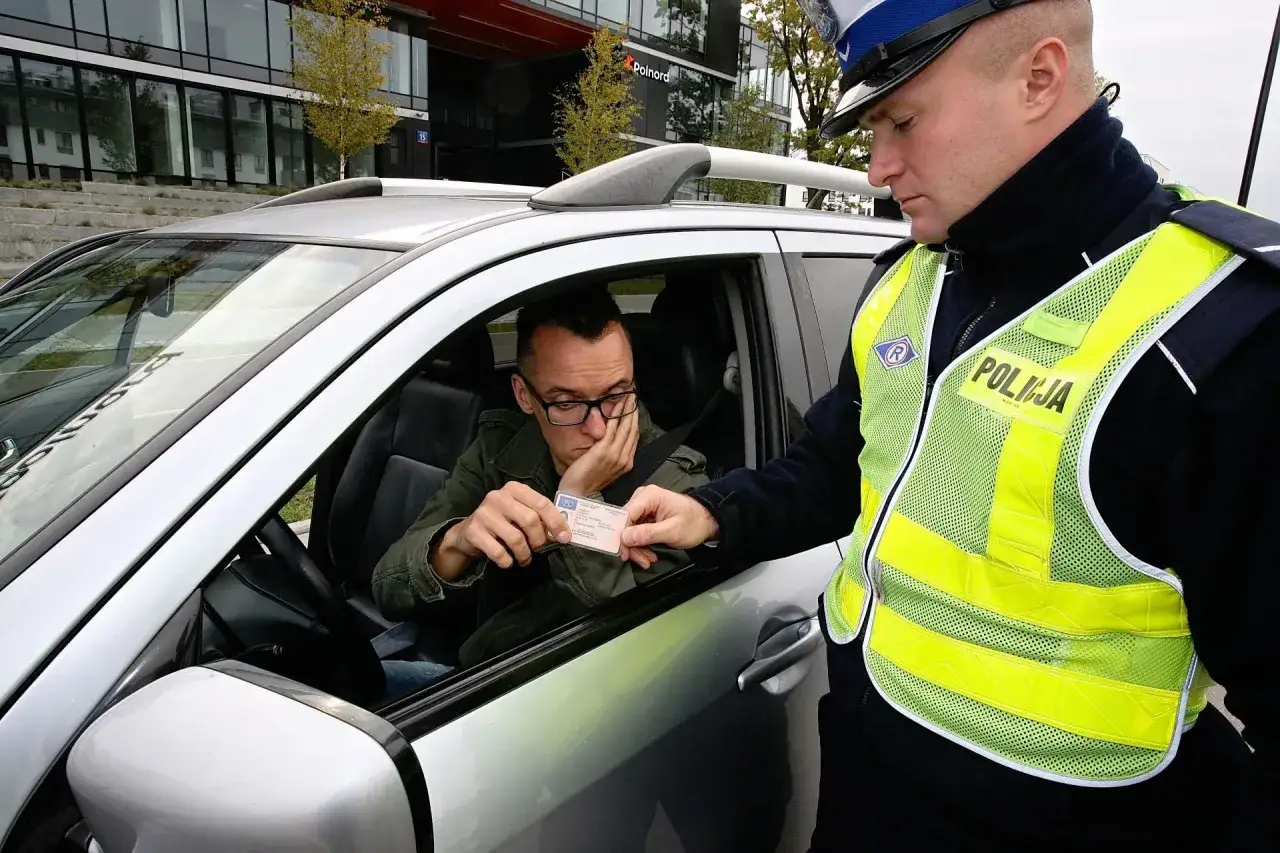 Policjant wręcza kierowcy mandat za brak prawa jazdy. Mężczyzna w okularach wygląda na zmartwionego.