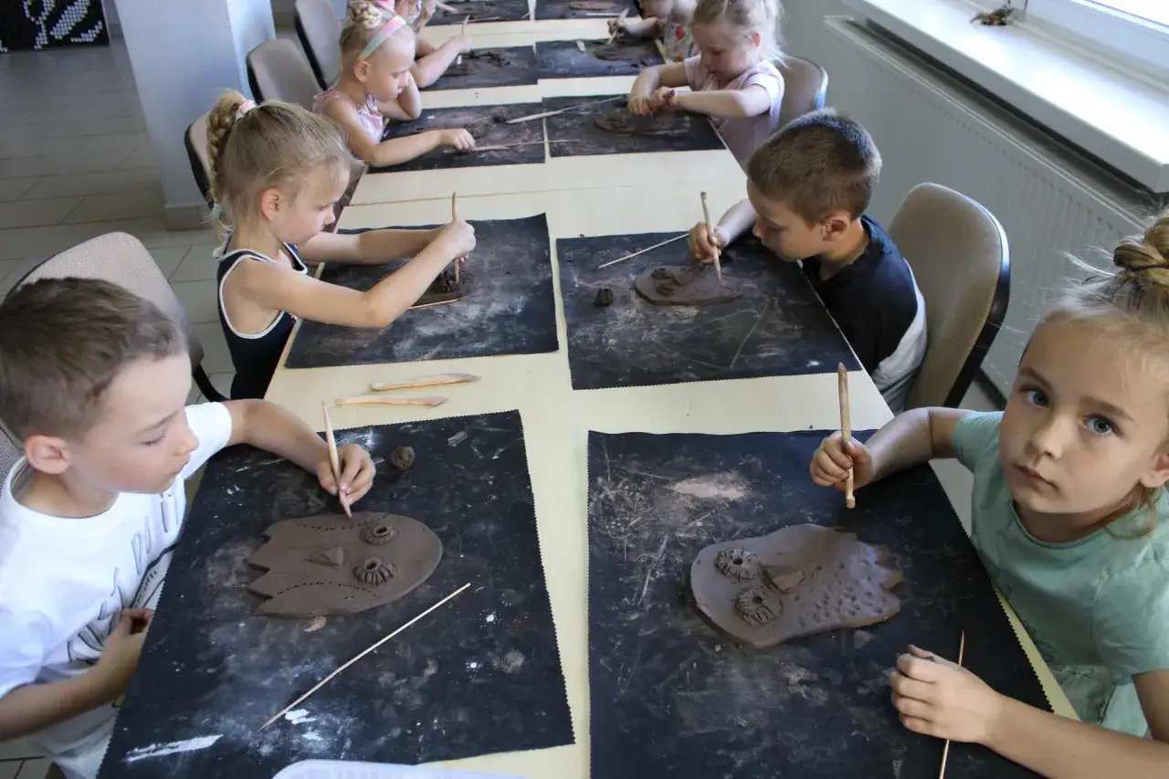 Dzieci tworzą fantastyczne stwory na warsztatach z gliny. Każde z nich skupione na swojej pracy, z patyczkiem w dłoni.
