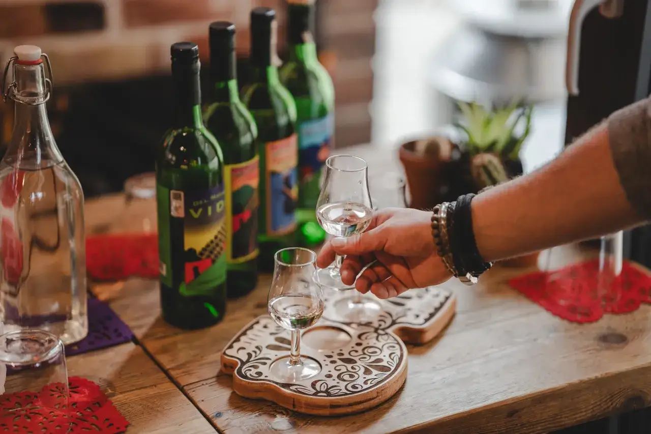 Degustacja: drink z mezcalem czy z tequilą? Na drewnianym blacie butelki i kieliszki z przejrzystym alkoholem.